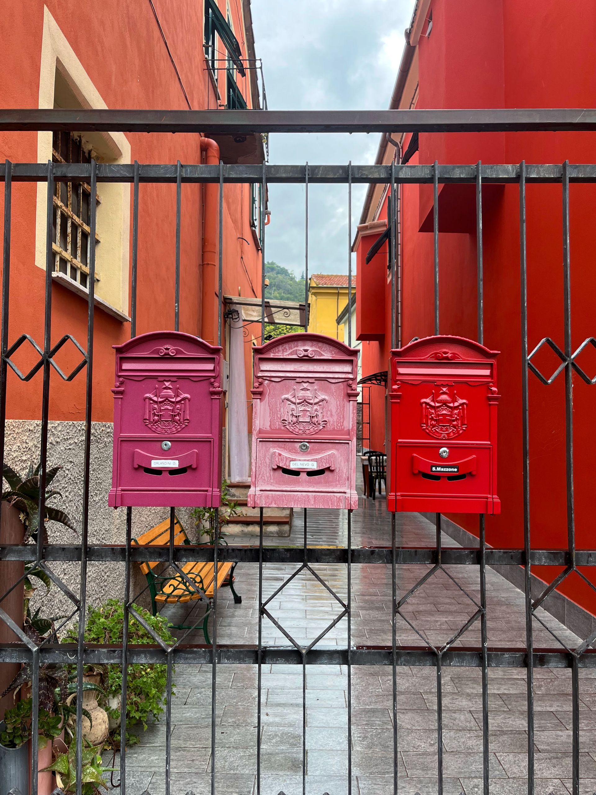 Three vibrant vintage mailboxes adorn an iron gate in a quaint alleyway, showcasing urban charm.